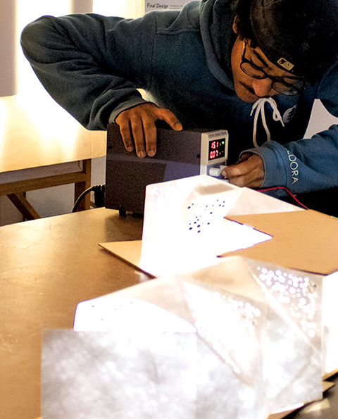 LET THERE BE LIGHT: Students in IDEA 292 Interdisciplinary Project Lab explore illumination through design of table-sized models. Ari Eaton ’24 designed an origami-based structure with frit patterning and custom circuit boards for mounting and powering LED lighting. Photo by Malcolm Davol ’24