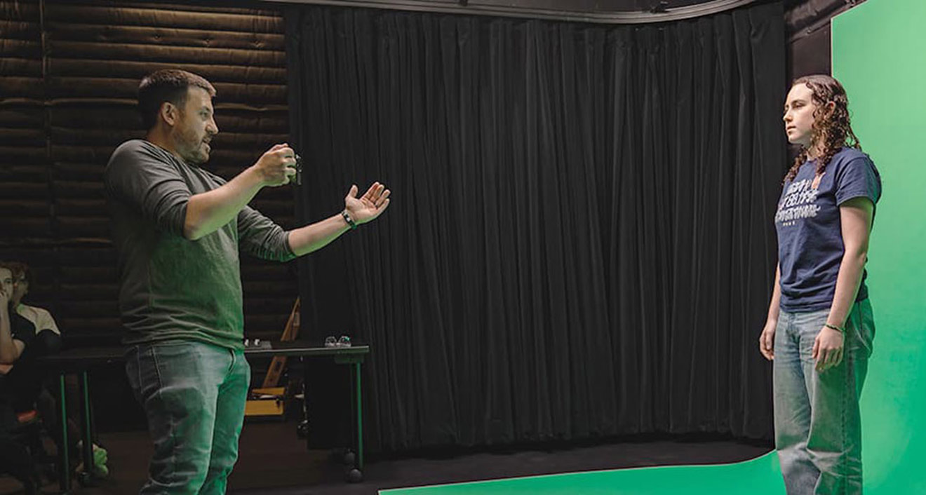 A student poses in front of a green screen during a visual effects demonstration at the Digital Design Commons