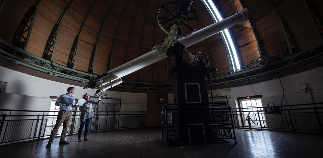 Two people stand beside the 20-inch Alvan Clark Great Refractor telescope inside the Van Vleck dome.