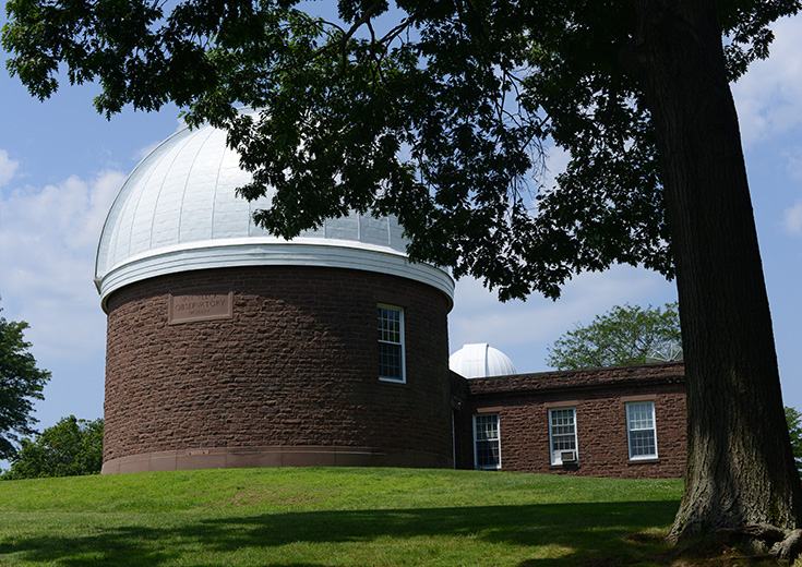 The Van Vleck Observatory building with a domed silver roof, situated on a grassy hill under a blue sky with scattered clouds.